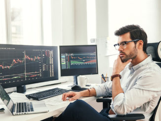 Young controller analyzing tables and graphs in front of several screens